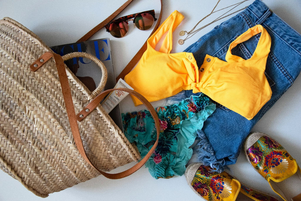 Summer clothing, shoes, accessories, and a tote bag laid out against a white background.